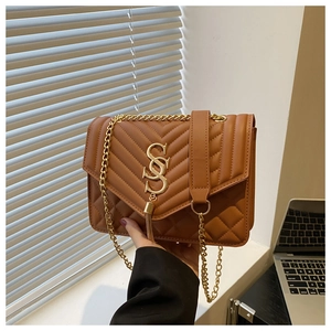Macro detail of brown quilted chain crossbody bag featuring a gold snake-shaped S buckle