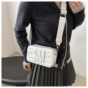 Close-up of a white quilted camera bag with SM logo and wide strap on model