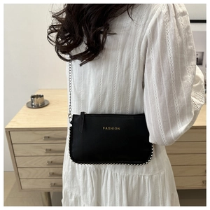 Detail of a black leather crossbody bag with golden Fashion text and metal bead trim