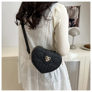 Detail of black heart-shaped quilted bag with gold heart lock shown on shoulder strap