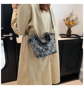 Detail of vintage floral embroidery on bucket bag with black leather handle and strap