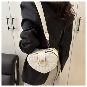 Detailed view of white heart-shaped quilted bag with gold lock and wide shoulder strap