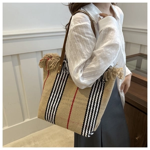 Detail of woven plaid tote bag featuring decorative fringe and brown leather straps