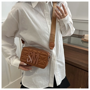 Detail of brown quilted camera bag with SM logo and wide fabric shoulder strap