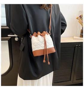 Close-up of drawstring bucket bag with quilted white leather and brown trim on a model