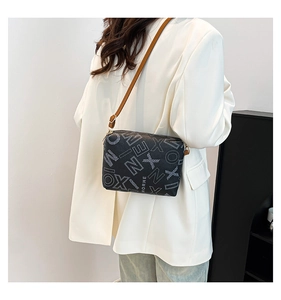 Detail of black tote bag with white typography and brown strap on a model shoulder