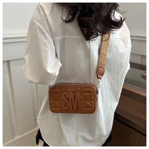 Detail of caramel camera bag showing quilted texture and broad patterned shoulder strap