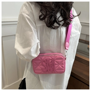 Detail of pink quilted camera bag with wide strap worn by a model in interior setting