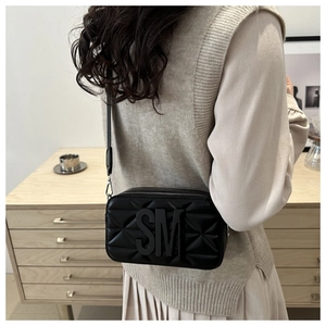 Detail view of a black quilted crossbody bag with metal letters and thin strap