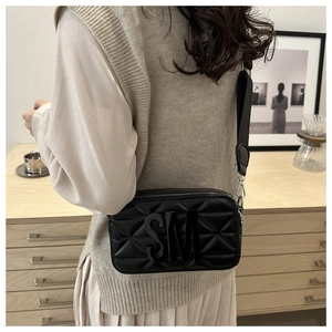 Detail of black crossbody bag featuring SM logo and wide fabric shoulder strap on model
