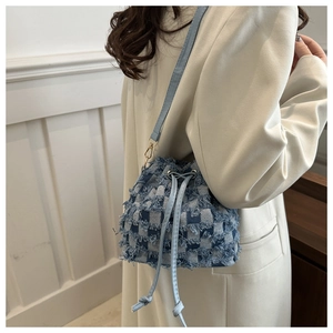 Detail of blue checkerboard denim bucket bag with frayed edges on beige blazer model
