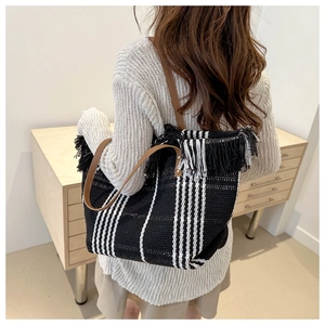 Detail view of striped canvas tote with fringe trim shown on a model's shoulder