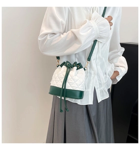 Detail of white quilted bucket bag with dark green leather trim and chain strap
