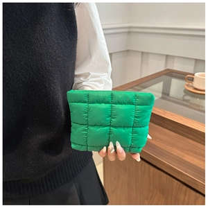 Close-up of a bright green puffy quilted nylon clutch held by a model in a cozy setting