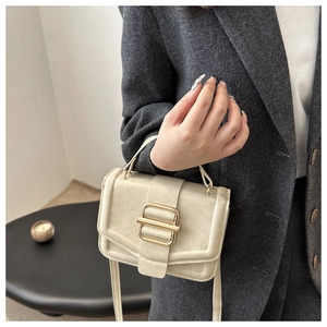 Detail of cream rectangular handbag with gold buckle and adjustable crossbody strap
