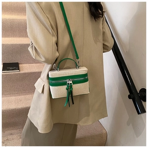 Detail of canvas box bag with green leather trim and tassel on a staircase background