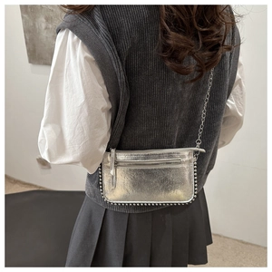 Close-up of silver crossbody bag with metallic rivets and sleek chain strap detail