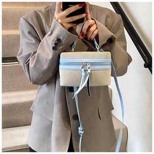Detail of blue and beige woven mini box bag featuring double zippers and leather tassels
