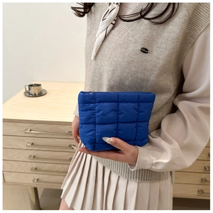 Blue quilted puff cosmetic bag held by a person against a minimalist home background
