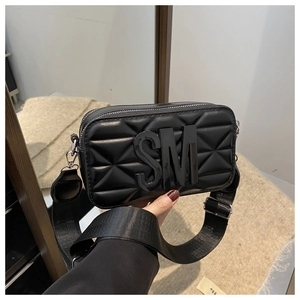 Detail of black camera bag with quilted triangle texture and wide fabric shoulder strap