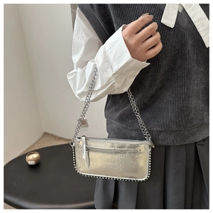 Detail of silver metallic crossbody bag featuring rivet edges and delicate chain strap