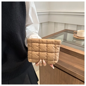 Detail of a brown quilted puffer clutch bag with square stitching and silver zipper