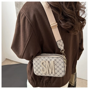 Detailed view of square camera bag with taupe pattern and wide fabric shoulder strap