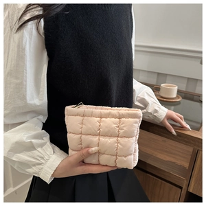 Close-up of light pink quilted makeup bag held in hand with golden zipper detail