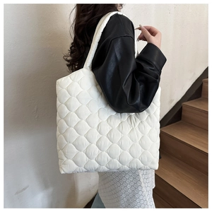 Detail of white quilted puffy bucket bag with thick padded strap worn by a model