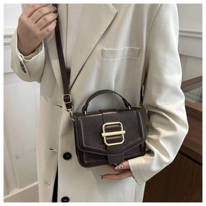 Détail d'un sac à bandoulière vintage marron foncé avec boucle dorée sur blazer blanc