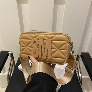 Quilted tan camera bag with wide strap and letter decoration shown in a stylish scene