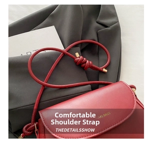 Detail of red leather crossbody bag with knot shoulder strap and gold metal tips