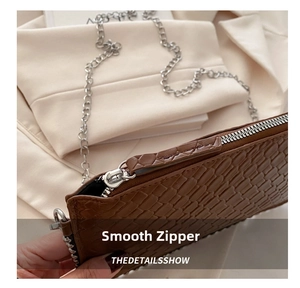 Detail of smooth silver zipper and embossed crocodile texture on a brown crossbody bag