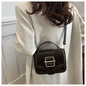 Detail of dark coffee leather handbag featuring a large golden rectangular metal buckle