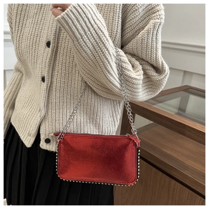 Detail shot of red metallic crossbody bag with silver rivets and metal chain strap