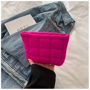 Detailed shot of a fuchsia quilted puffy cosmetic bag held against a denim jacket