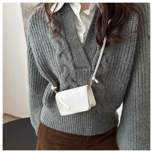 Dettaglio di una mini borsa a tracolla bianca con finiture dorate su un maglione grigio