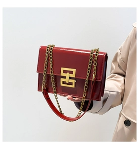 Detail of red patent leather rectangular crossbody bag with gold geometric buckle and chain