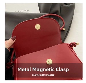 Close-up of a golden magnetic snap closure on a dark red leather crossbody bag