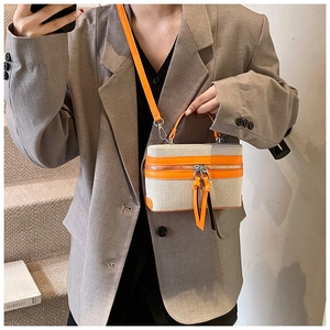 Detail of a color-block canvas box bag with orange leather trim on a model