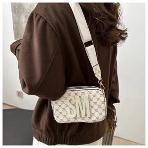 Close-up of cream camera bag with retro monogram pattern and wide adjustable strap