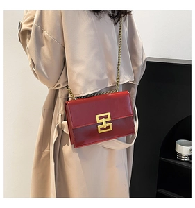 Detail of red glossy leather shoulder bag with gold chain strap and stylish metal clasp