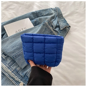 Detail of bright blue quilted cosmetic bag with puffy checkered texture on white sheets