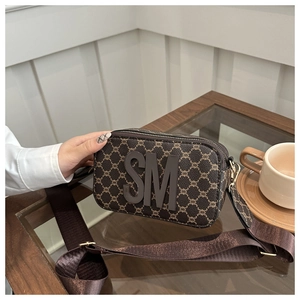 Macro detail of dark brown textured camera bag featuring a bold 3D SM letter emblem
