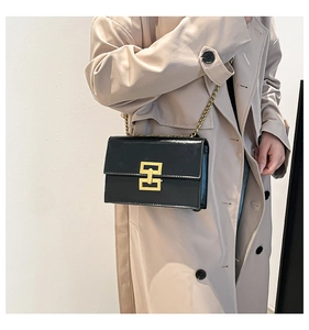 Detail of a black leather crossbody bag with a gold interlocking clasp and chain strap