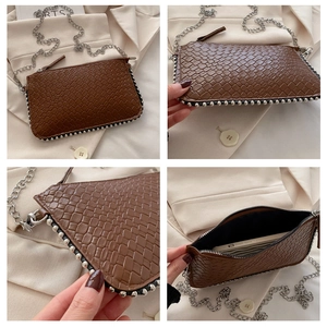 Detail of crocodile embossed texture and silver ball rivets on a brown chain tote bag