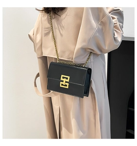 Detail of black box-shaped leather shoulder bag with gold chain and metal buckle