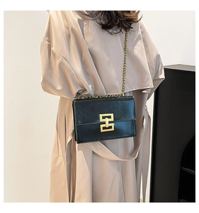 Close-up of black glossy leather shoulder bag featuring gold chain and H-shaped buckle