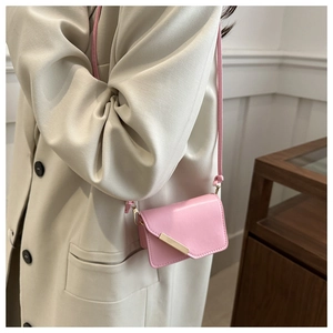 Dettaglio mini borsa a tracolla rosa con barra dorata indossata su un blazer beige