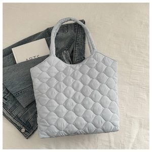 Close-up of light blue quilted tote bag on white textured surface with casual props